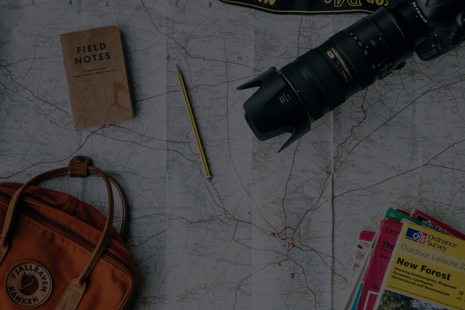 Eine Landkarte, auf der eine Kamera, ein Rucksack, ein Stift und Notizbücher liegen