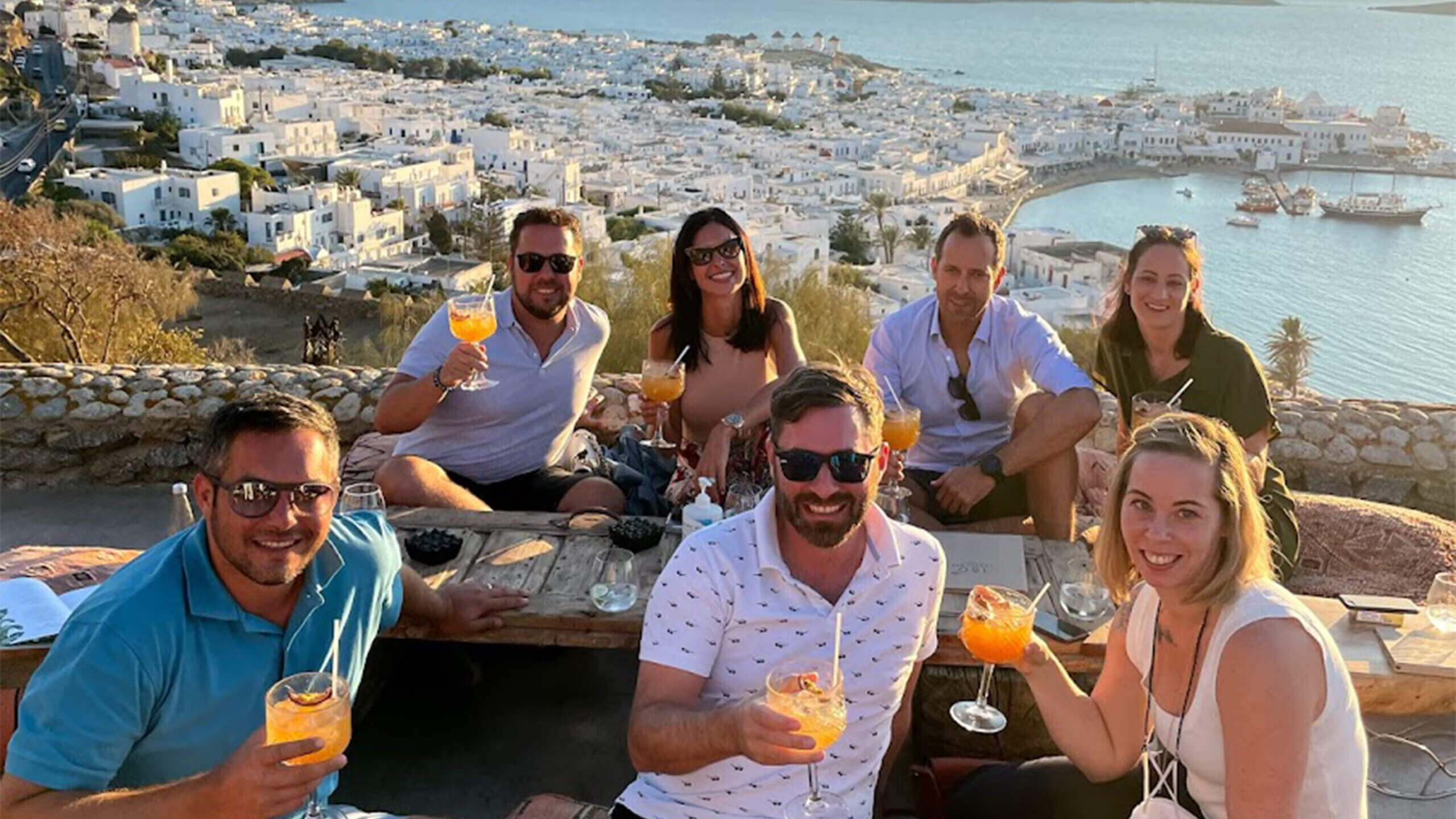 Eine Gruppe Männer und Frauen mit Cocktails - im Hintergrund die Aussicht auf eine Küstenstadt