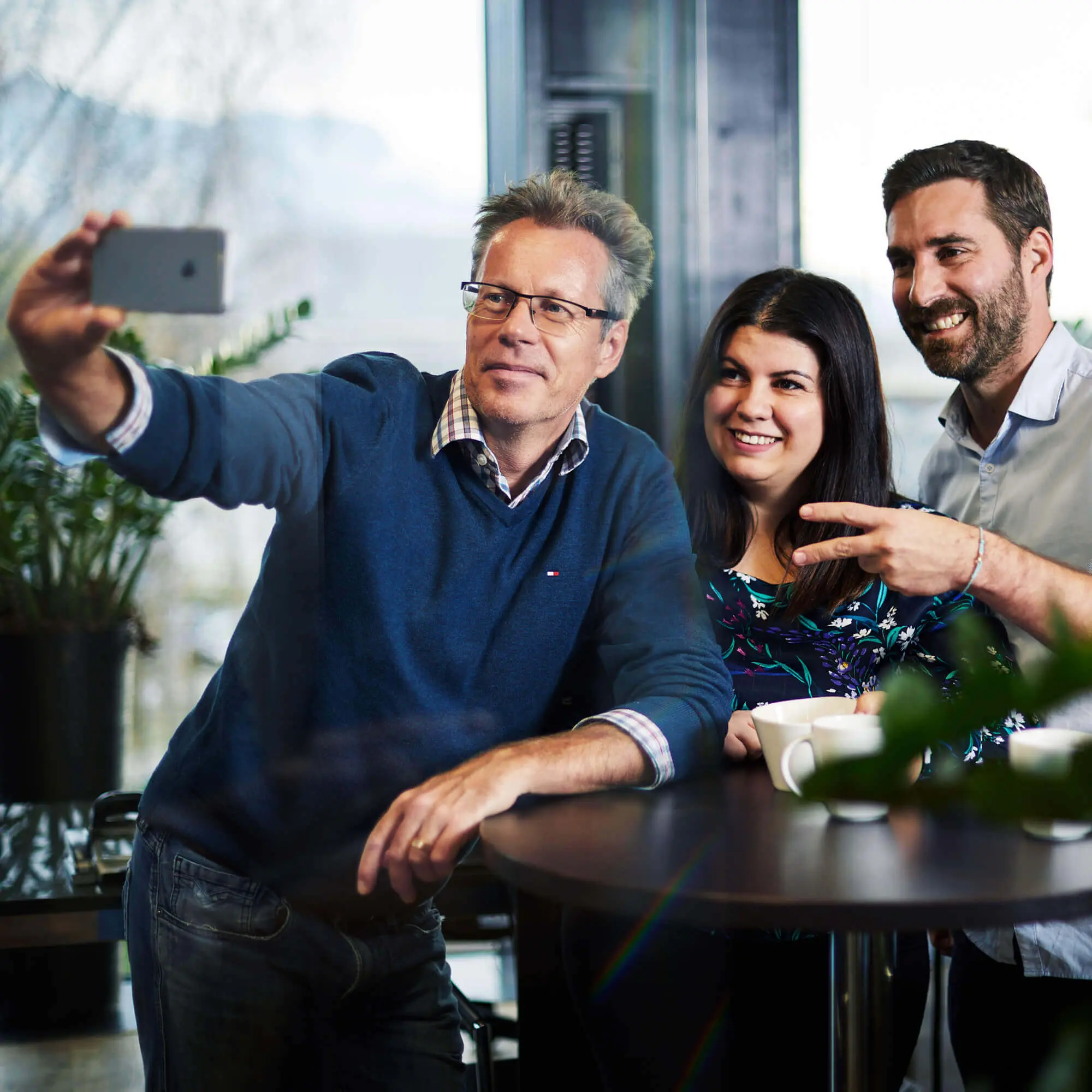Zwei Männer und eine Frau die ein Selfie mit dem Handy im Büro machen