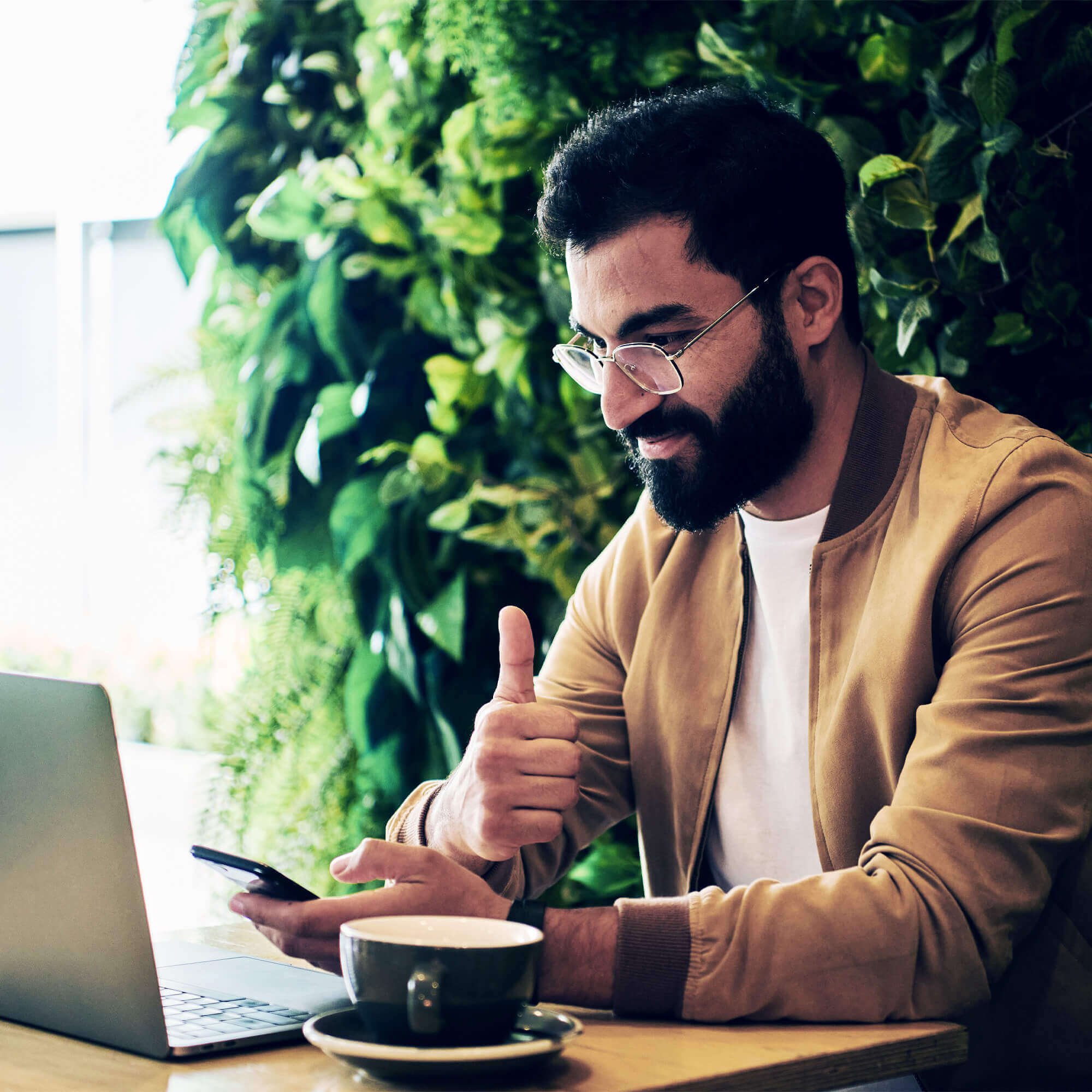 Mann mit Bart und Brille am Laptop mit Kaffee
